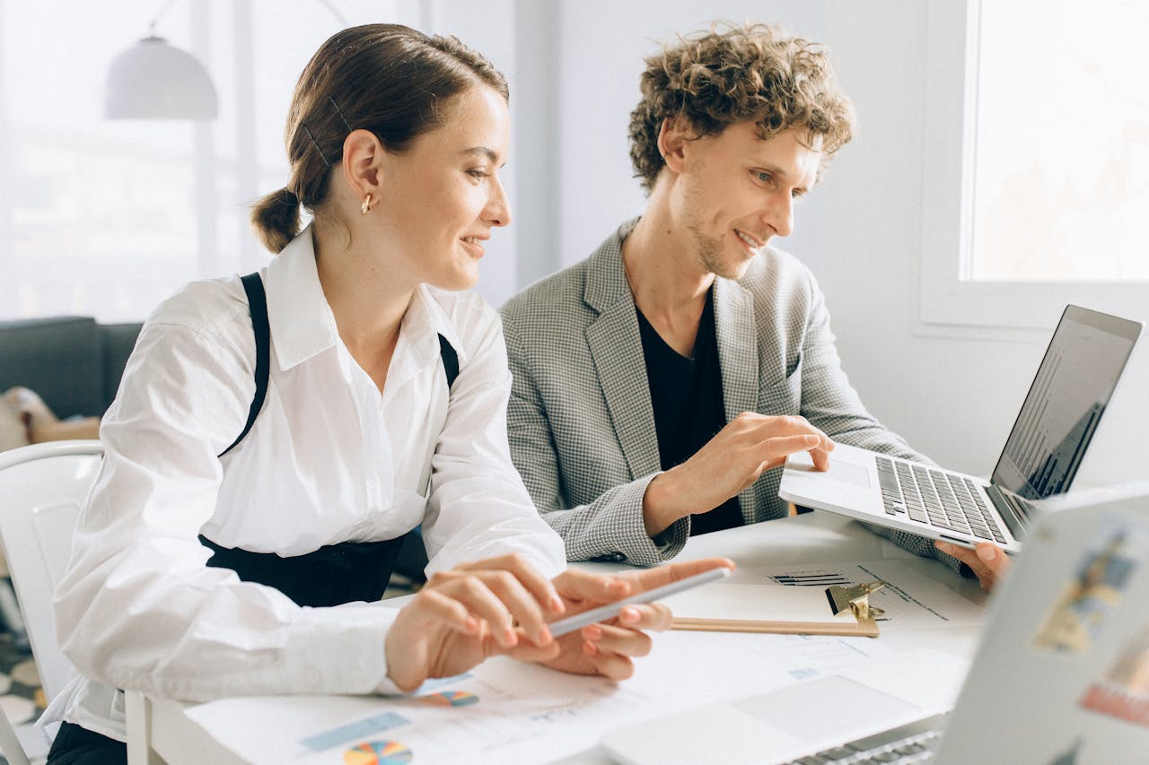 Two colleagues collaborating on a project, using laptops and documents in a modern office setting.